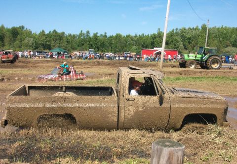 1979 Ford F-150 - A muddy pickup truck is stuck in a mud pit during an event, with spectators and other vehicles in the background.