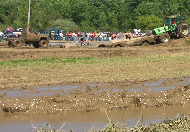 Mud-covered trucks stuck in a muddy field, with a tractor pulling one