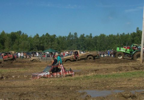 1979 Ford F-150 - Multiple trucks are stuck in the mud during a competition, with a tractor assisting.