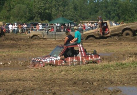 1979 Ford F-150 - Several trucks are stuck in a mud pit during an event, with spectators in the background.