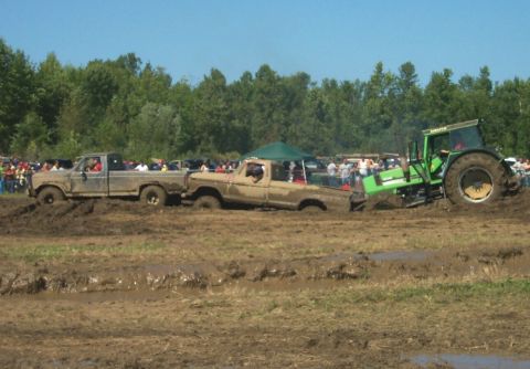 1979 Ford F-150 - Two trucks are stuck in a mud pit, with a tractor attempting to pull one out during an event.