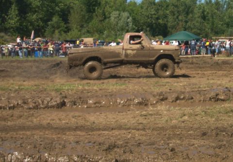 1979 Ford F-150 - A truck navigates a muddy track during an event, with a crowd gathered to watch.