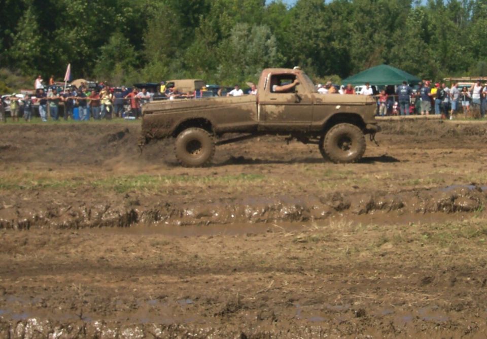 Muddy pickup truck driving through a mud pit with spectators watching