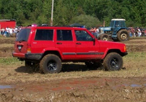 1979 Ford F-150 - A red Jeep Cherokee navigates a muddy terrain, while a blue tractor is visible in the background.