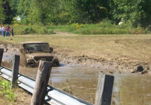 1979 Ford F-150 - A Jeep Wrangler navigates a muddy obstacle course, with spectators watching from the side.
