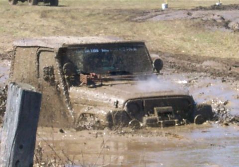 1979 Ford F-150 - A Jeep is stuck in a mud pit, with steam rising from the engine area.