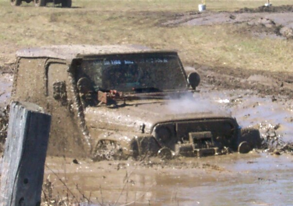 Jeep deep in mud, steam coming off hood. Another vehicle visible in background