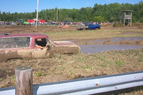 1979 Ford F-150 - A red SUV is stuck deep in the mud during an event, with spectators and other vehicles visible in the background.