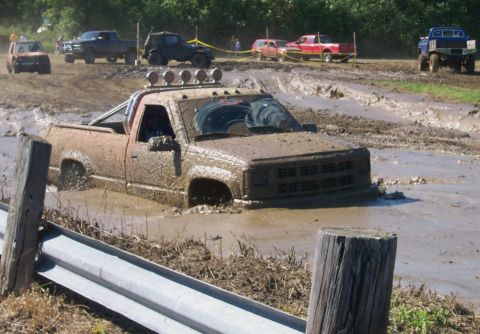 1979 Ford F-150 - A truck is stuck deep in a mud pit during an off-road event, with other vehicles visible in the distance.