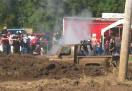 1979 Ford F-150 - A pickup truck is stuck in a mud pit during a competition, with spectators gathered around.
