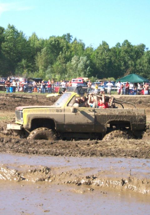 1979 Ford F-150 - A lifted pickup truck navigates a muddy obstacle course with spectators in the background.