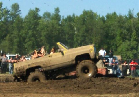 1979 Ford F-150 - A lifted truck is stuck in a mud pit during an event, with onlookers gathered around.