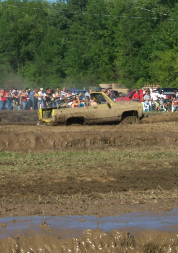 Yellow pickup truck stuck in mud, people watching in background