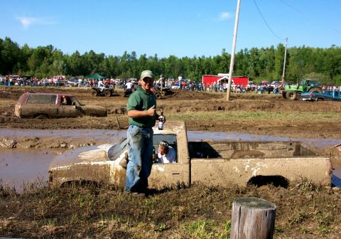 1979 Ford F-150 - A muddy pickup truck is stuck in a mud bog during an event, with spectators and other vehicles in the background.
