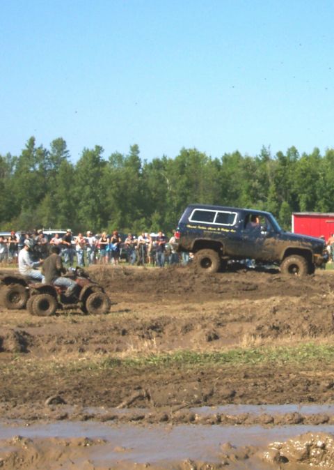 1979 Ford F-150 - ATVs and a 4x4 SUV navigate a muddy track during a competition with spectators in the background.
