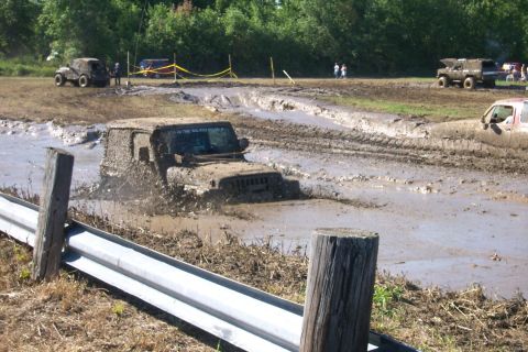 1979 Ford F-150 - Multiple off-road vehicles struggle through a muddy track during an event.