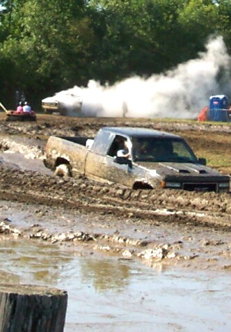 1979 Ford F-150 - A truck is stuck in a mud pit while another vehicle in the background creates a large cloud of smoke.