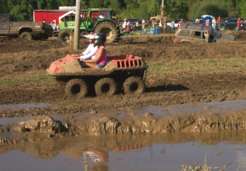 1979 Ford F-150 - An all-terrain vehicle navigates a muddy track, with other vehicles and spectators in the background.