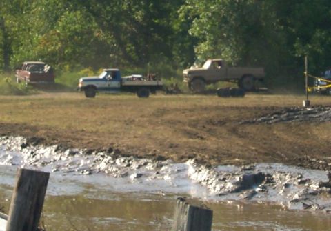 1979 Ford F-150 - Several trucks are in a muddy field, with trees in the background.