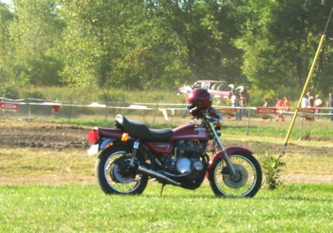 1979 Ford F-150 - A motorcycle sits on a grassy field with a dirt track and spectators in the background.