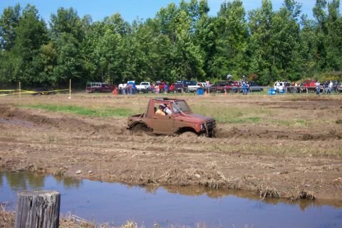 1979 Ford F-150 - A Suzuki Samurai navigates a muddy obstacle course with spectators and other vehicles nearby.