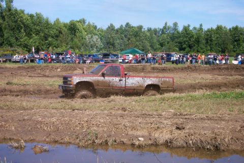 1979 Ford F-150 - A red and white pickup truck is stuck in the mud during a competition, with spectators in the background.