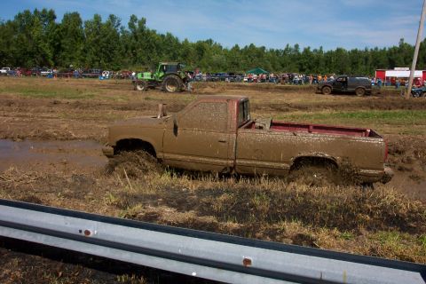 1979 Ford F-150 - A muddy pickup truck is stuck in a mud pit during an event, with a tractor and spectators visible in the background.