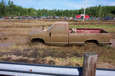 1979 Ford F-150 - A truck is stuck deep in the mud at an outdoor event with many people watching.