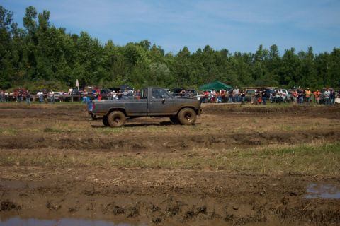 1979 Ford F-150 - A gray pickup truck navigates a muddy track with spectators watching in the distance.