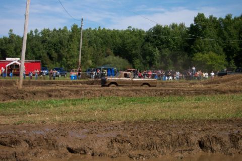1979 Ford F-150 - A pickup truck navigates a muddy track during an event, with onlookers gathered in the background.