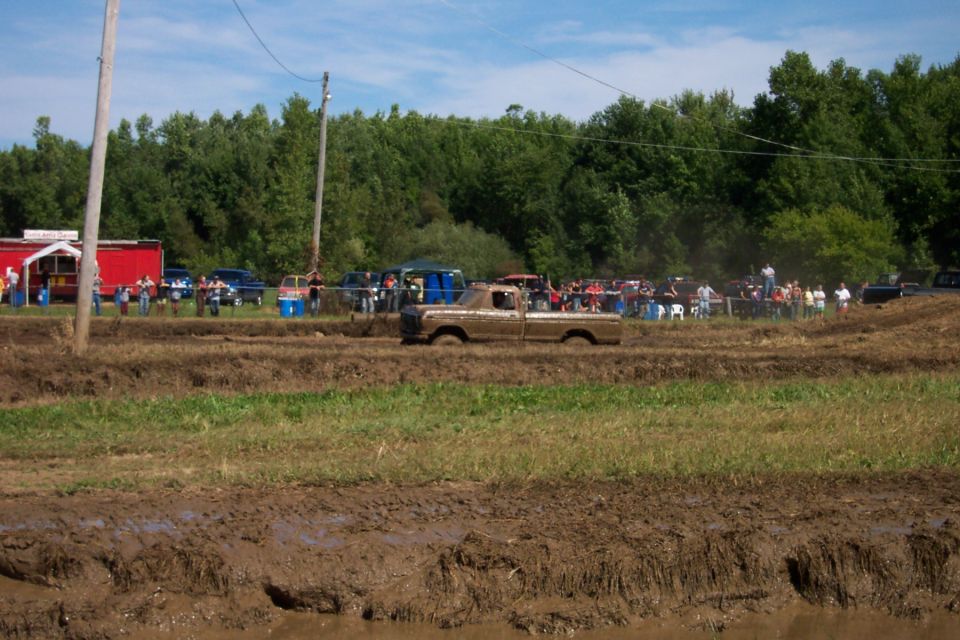 Brown pickup truck stuck in mud pit with spectators watching