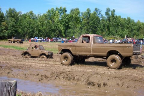 1979 Ford F-150 - Two trucks are participating in a mud bogging event, with spectators watching from the sidelines.