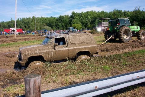 1979 Ford F-150 - A mud-covered SUV is stuck in a mud pit and being pulled out by a green tractor during an event.
