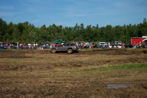 1979 Ford F-150 - A Jeep Grand Cherokee navigates a muddy track during an event, with a crowd watching.