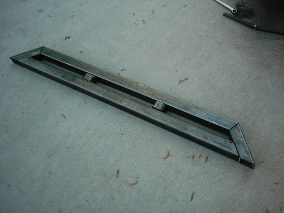 Metal bracket with two rectangular cutouts, lying on a concrete floor