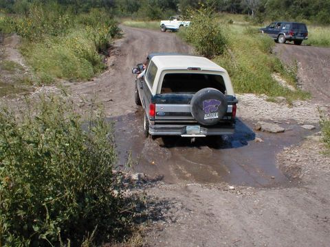 1994 Ford Bronco - A Ford Bronco navigates a muddy off-road trail with other vehicles in the background.