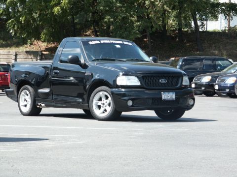 2001 Mercury Grand Marquis - A black Ford F-150 SVT Lightning pickup truck is parked in a lot, with other vehicles visible in the background.