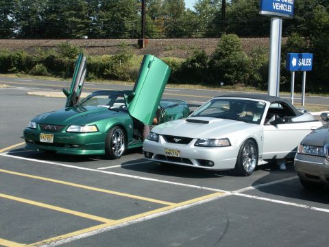 2001 Mercury Grand Marquis - Two Ford Mustang convertibles, one green with lambo doors and one silver, are parked side-by-side at a car show.