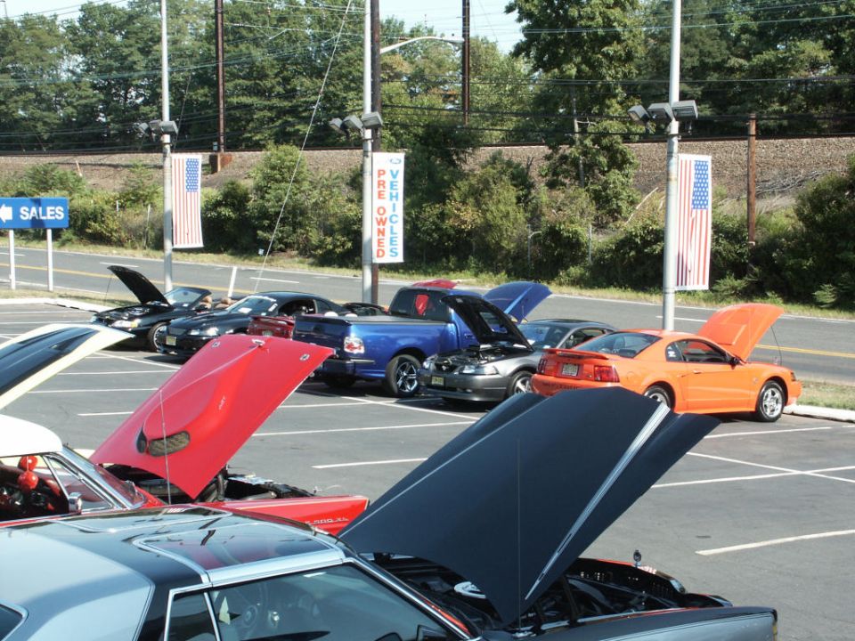 Cars parked in lot with hoods up, some with American flags on poles