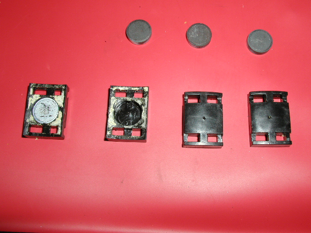 Four black plastic brackets with round rubber insert pucks laid out on red surface