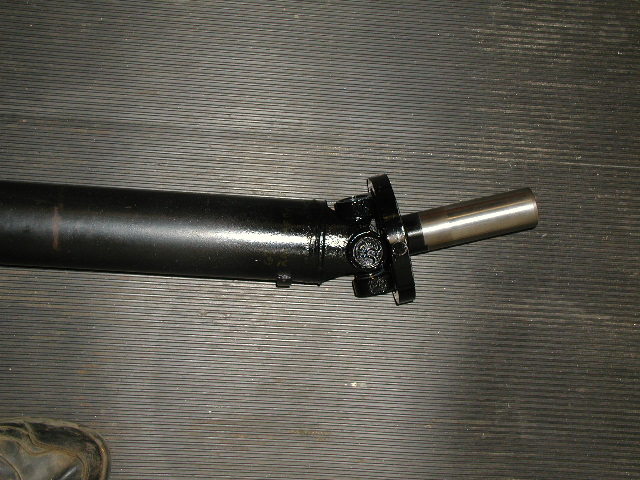 Black steel driveshaft with U-joint and slip yoke on a workbench surface