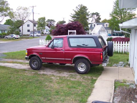 1995 Ford Bronco - A red Ford Bronco with a black top is parked in a residential driveway.