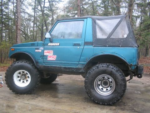 1987 Suzuki Samurai - Modified 1987 Suzuki Samurai with off-road tires and custom wheels parked outdoors.