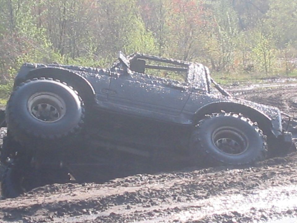 Mud-covered lifted Suzuki Samurai sunk to the axles in a mud pit on oversized mud tires
