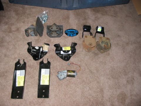 1991 Ford Bronco - Assorted vehicle brackets and a motor are laid out on a carpeted floor, likely for sale or inventory.