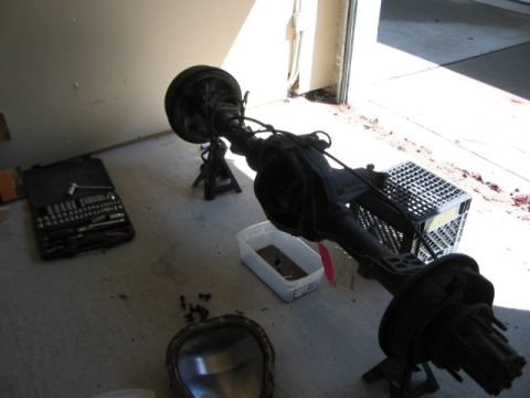 1991 Ford Bronco - A disassembled vehicle rear axle assembly is shown in a garage setting, with tools and parts laid out.