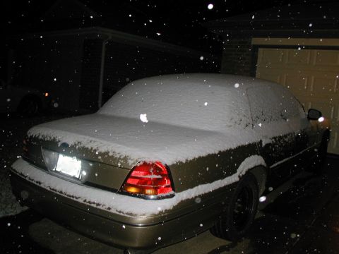 2000 Ford Crown Victoria - A gold sedan is parked in front of a garage during a snowfall.