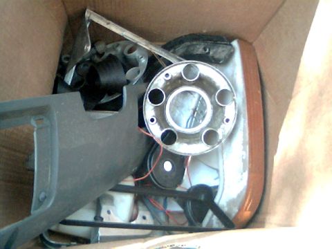 1992 Ford F-150 - A collection of vehicle parts, including a hubcap and a headlight assembly, are stored inside a cardboard box.
