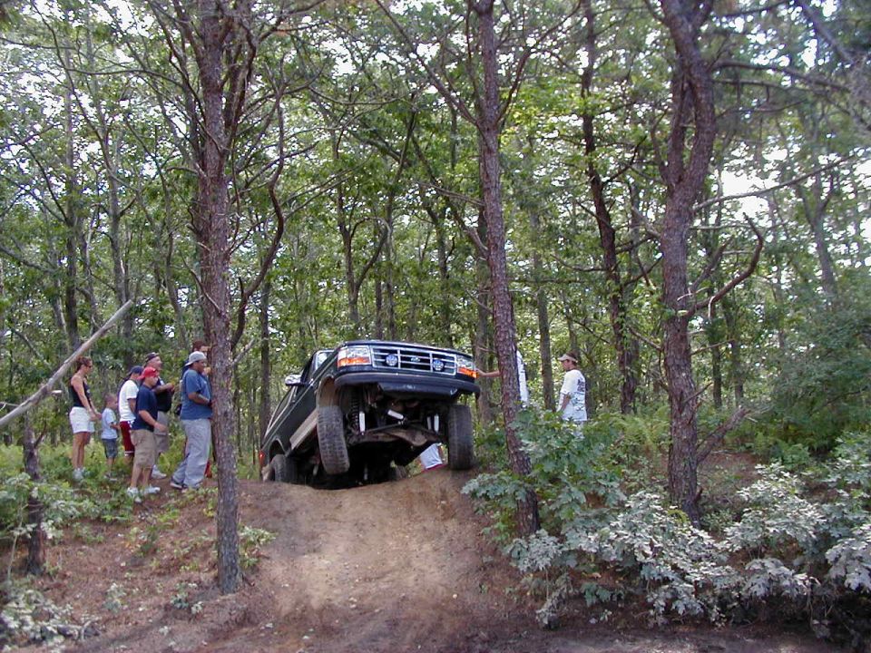 Lifted green Ford Bronco cresting a steep sandy trail hill with spectators watching