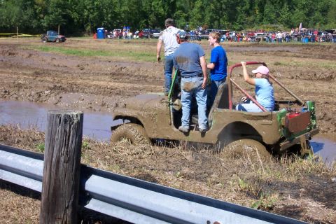 1979 Ford F-150 - Vintage Jeep stuck in mud during a bogging event. Spectators and other vehicles are in the background.